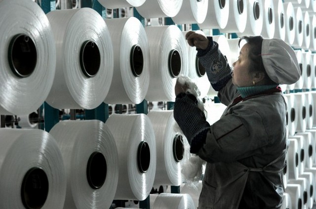 Рабочая проверяет машину, которая производит одеяла на экспорт на заводе в китайской провинции Чжэцзян, 12 января 2015 года