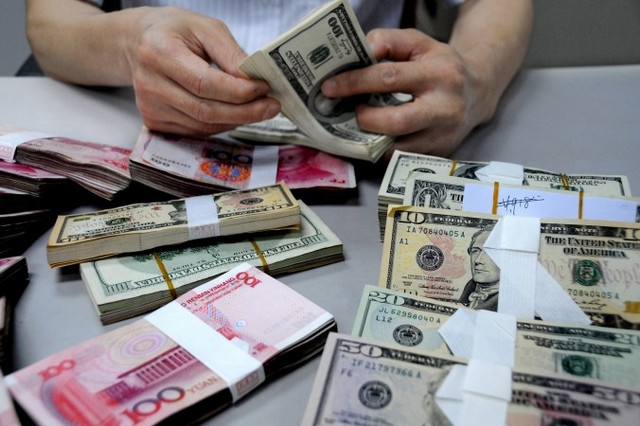 Китайский клерк подсчитывает доллары США рядом с пачками китайских юаней в филиале Банка Китая, Ляньюньган, провинция Цзянсу, Китай