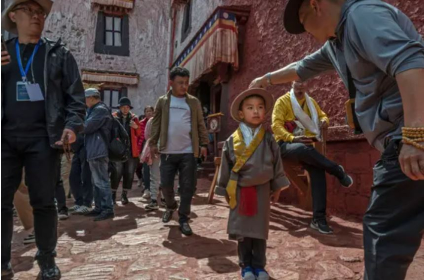 Тибетський буддист поправляє капелюх хлопчикові в традиційному одязі під час відвідування палацу Потала, об'єкта Всесвітньої спадщини ЮНЕСКО, під час організованого урядом візиту в Лхасі, Тибет, Китай, 16 червня 2023 року. (Kevin Frayer/Getty Images)