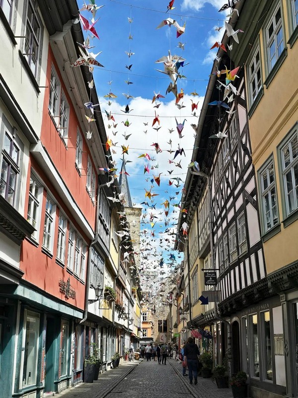 Люди прогулюються по барвистому Кремербрюкке (Містку купців) в Ерфурті, Німеччина. Кафе, художні галереї та бутики, що продають вироби народних майстрів, вишикувалися вздовж брукованої вулиці шириною 18 футів. (Rigorius/CC BY-SA 4.0)