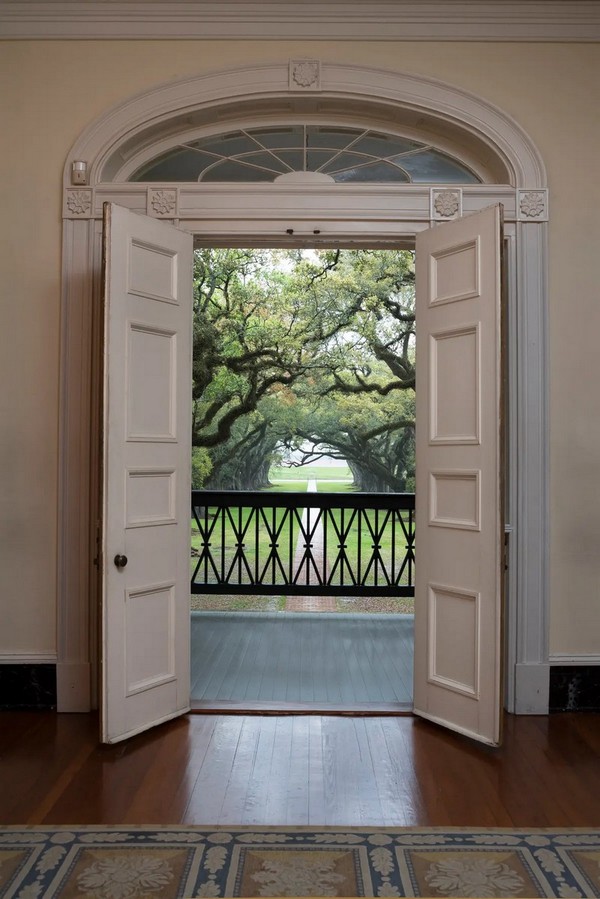 Панельная дверь особняка плантации Оук-Элли расположена под арочным транцемом в виде солнечного луча с лепниной в виде розетки вместо заключительного камня. Дверные коробки также украшены резьбой в форме розеток. С открытой двери открывается вид на деревянные перила из пшеничных колосьев, простирающихся вдоль верхних балконов особняка. (Oak Alley Foundation)