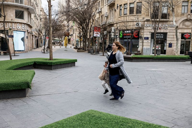 ​Жінка з дитиною біжать до укриття, коли в Єрусалимі лунають сирени, 28 лютого 2026 року. (John Wessels / AFP via Getty Images)
