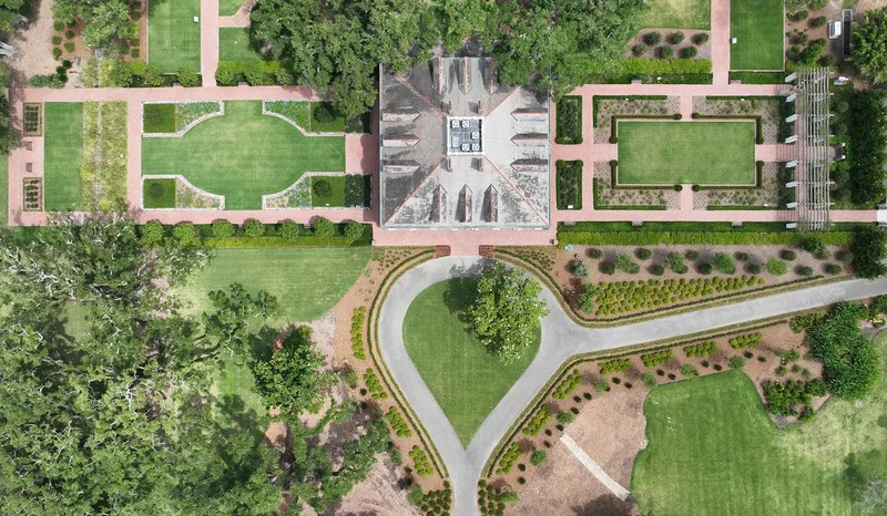 Раскидистые симметричные сады с обеих сторон особняка включают ухоженные газоны, зрелые деревья и цветники. С высоты птичьего полета симметрия особняка становится очевидной: по три двускатных мансардных окна с каждой стороны квадратной конструкции. (Oak Alley Foundation)