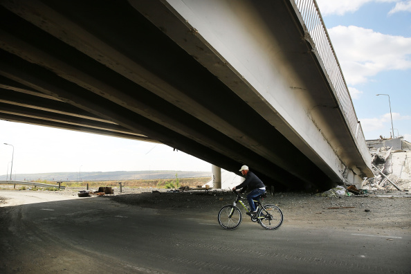 Чоловік проїжджає на велосипеді під зруйнованим мостом в Луганську, 13 вересня 2014 року. Фото: Spencer Platt/Getty Images