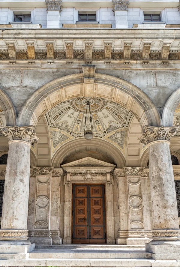 В Угорській державній опері симетрія помітна з будь-якого ракурсу. Цей пишно різьблений вхід, обшитий європейським дубом, під класичним фронтоном і аркою, пропорційно розташований між двома пілястрами з капітелями у формі кола та півкола. Ці елементи розташовані точно між двома вапняковими колонами з коринфськими капітелями, облямованими в основі каменем та розетками. Внутрішня частина купольної стелі прикрашена барвистими майоліковими (італійськими керамічними) орнаментами, які контрастують з точно розташованими арками, обшитими панелями. (Claude Huot/Shutterstock)