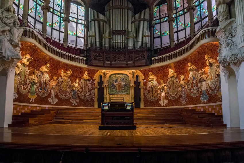 Готичні скульптури з музичними інструментами утворюють півколо за сценою і розділені на дві групи каталонським гербом у центрі. Верхня частина скульптур виринає з мозаїчної стіни за ними, на якій переважають червоні та помаранчеві плитки. Над сценою розташована галерея, що нагадує церковний хор, в якій знаходиться орган з понад 3000 труб. (goga18128/Shutterstock)