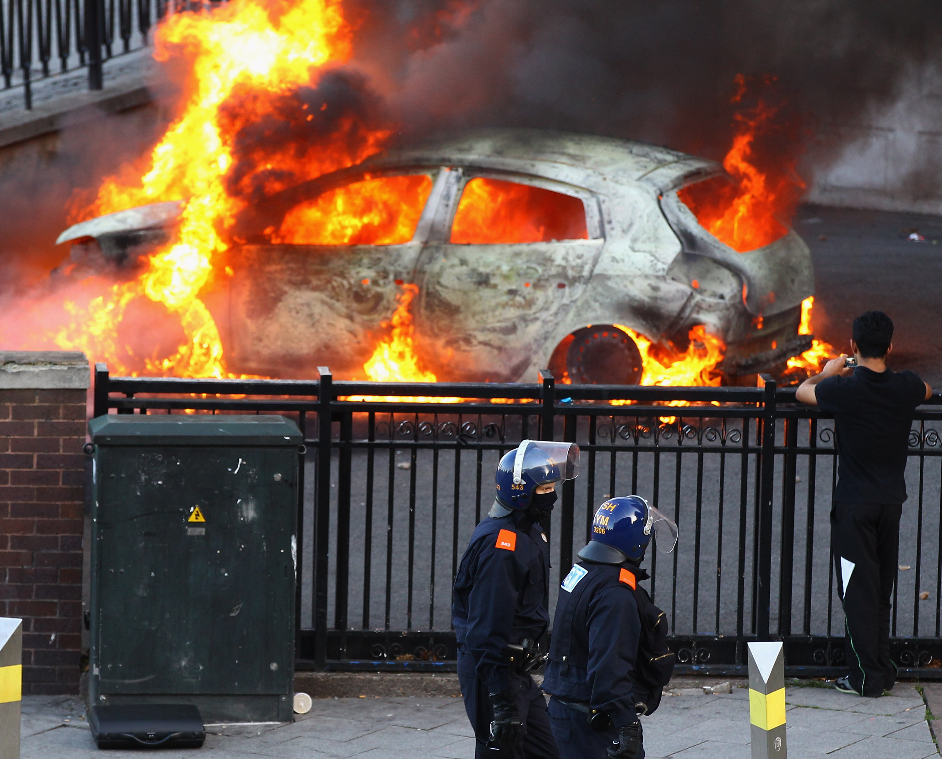 Полиция проходит возле горящей машины, которую подожгли хулиганы в центре города Бирмингема 8 августа 2011 года. Фото: Jeff J Mitchell/Getty Images