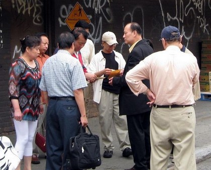 Неподалёку от места событий – района Flushing, неизвестный китаец в костюме выдаёт деньги активным участникам группы поддержки компартии. Фото предоставлено жителем Нью-Йорка