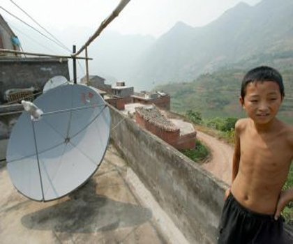 Маленький китайський хлопчик стоїть на даху свого дому біля супутникової тарілки в новому селі мігрантів Гуйхуа. Сім’ї, на зразок його, 16 червня були позбавлені можливості приймати сигнал ТБ НДТ. Фото: Goh Chai Hin/AFP/Getty Images