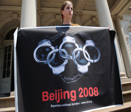 Женщина держит плакат с изображением олимпийских колец в виде наручников во время демонстрации в защиту прав человека на ступеньках здания городского совета Нью-Йорка. Фото: Don Emmert/AFP/Getty Images