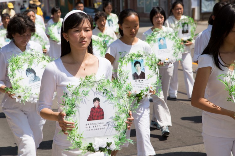 Практикующие Фалуньгун в Торонто, Канада, 20 июля 2012 года, одетые в белый цвет, символизирующий в Китае скорбь. Они несут в руках фотографии последователей практики, которые были замучены в КНР до смерти. Фото: Evan Ning/The Epoch Times