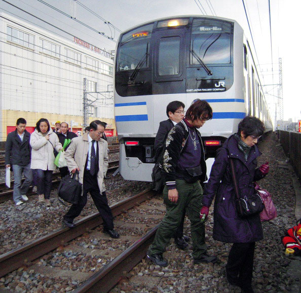 Люди переходять через залізничні колії після зупинки руху приміських поїздів у місті Funabashi, передмісті Токіо після сильного землетрусу в Японії 11 березня 2011 року. Фото: AFP PHOTO / Jiji press