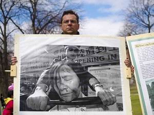 Пытки КПК: Майкл Картер держит плакат, на котором изображена инсценировка пыток, которым в настоящее время подвергаются последователи Фалуньгун в Китае. Фото: Риордан Галлючио/Великая Эпоха