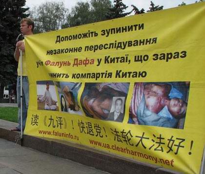 Последователь духовной практики Фалуньгун держит плакат с фотографиями жертв пыток и насильственного извлечения органов. Фото: The Epoch Times