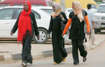 Суданські жінки. Одна з них у брюках і в довгій чорній сукні йде по вулиці Хартума. Тисячі жінок у штанях кожен день ходять вулицями столиці, ризикуючи отримати прочухана, якщо поліція знайде їхній одяг провокаційним. Фото: Ashraf Shazly/AFP/Getty Images 