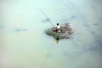 Китай. Людина сидить на мілині і ловить рибу в каламутній воді озера. Фото: China Photos/Getty Images