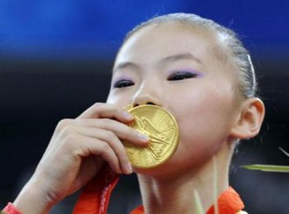 Китаянка Хэ Кесинь целует свою золотую медаль 18 августа 2008 г. после победы в соревнованиях на брусьях. Ян Илинь выиграла «бронзу». Обе китайские гимнастки подозреваются в том, что не достигли допустимого возраста для участия в Олимпийских играх. Фото: 