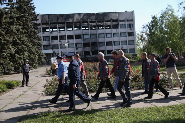 Сталевари Маріуполя і місцевий патруль міліції проходять повз частково згорілої будівлі міськради 16 травня 2014 р. Цього ж дня робітники організували бригади, щоб витісняти з адмінбудівель сепаратистів. Фото: John Moore/Getty Images