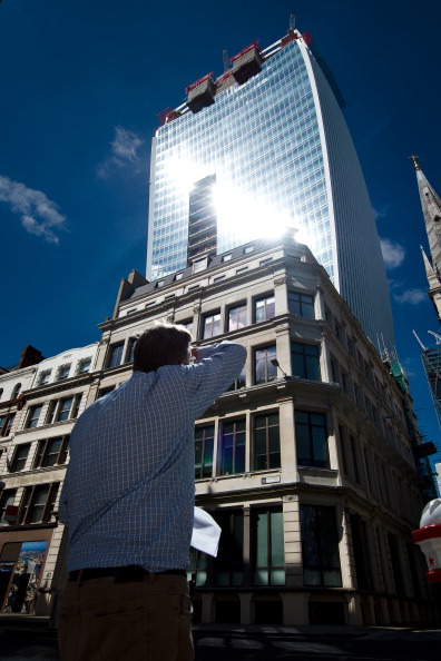 Мужчина закрывает глаза рукой от сильного света, отражённого окнами строящейся высотки «Уоки-токи. Фото: LEON NEAL/AFP/Getty Images
