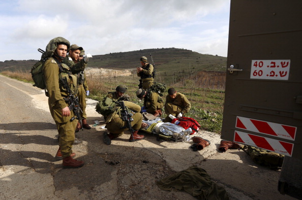 Израильские солдаты готовятся эвакуировать раненого товарища в результате взрыва на оккупированных Голанских высотах 18 марта 2014 г. в районе села Мадждаль Шамс. Фото: JALAA MAREY/AFP/Getty Images