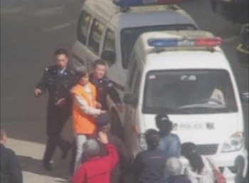 После суда Ху Цили в наручниках сажают в полицейскую машину. Перед машиной её родственники и пожилая мать (в красной одежде). Фото с epochtimes.com 