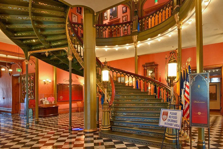 Вишукані гвинтові сходи, виготовлені з чавуну, зустрічають кожного, хто входить до Старого Капітолію штату Луїзіана. Декоративні повторювані вирізи окреслюють сходинки, а балясини мають форму готичних віконних рам. Розетки прикрашають сходинки, а латунні ліхтарі увінчують баштоподібні стовпи. Чавунні колони, розписані сусальним золотом, оточують сходи. Чорно-біла мозаїчна мармурова підлога поєднується з чавуном. (Jim Vallee/Shutterstock)