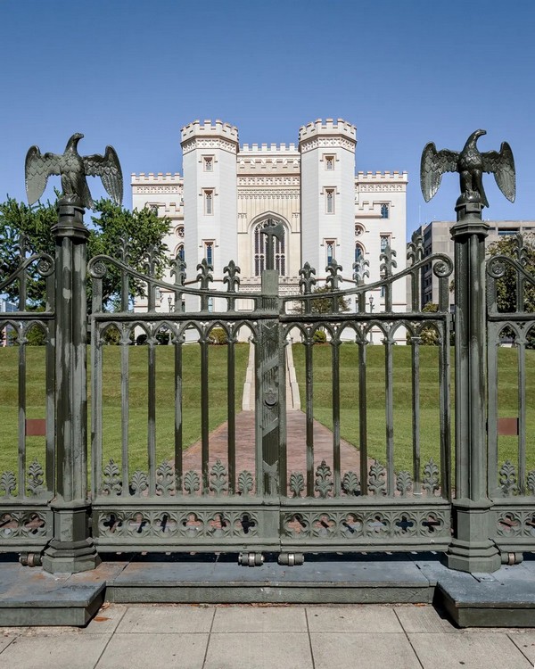 Капітолій оточує 1,8-метрова залізна огорожа з трьома воротами на західному, північному та східному входах. Ворота прикрашені стовпчиками-навершями у формі орлів. Огорожа також має чотирилисник та впізнавану лілію (флер-де-ліс), яка виникла у Франції як стилізована лілія. Через французьку спадщину штату, лілія (флер-де-ліс) стала офіційним символом Луїзіани. (George Howard Jr/Shutterstock)