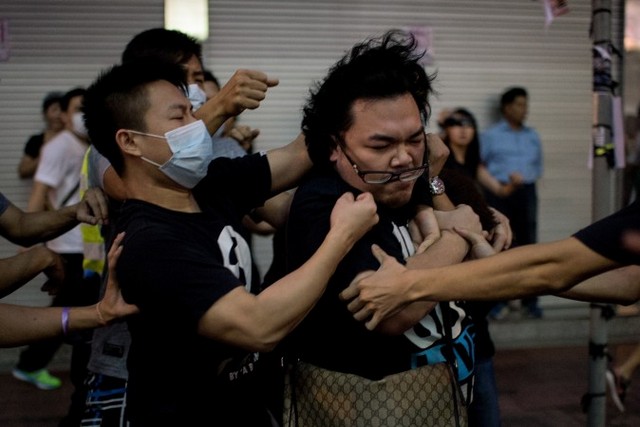 Группа людей в масках избивает мужчину (справа), который попытался помешать им убрать баррикады на месте проведения демократического протеста в районе Козуэй Бэй Гонконга, 3 октября 2014 года. По информации источников, глава администрации Гонконга Лян Чжэньин нанял мафиозные группировки, чтобы те нападали на протестующих. Фото: Alex Ogle/AFP/Getty Images