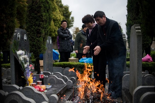 Супруги молятся и сжигают бумагу во время ежегодного праздника Цинмин, или Дня уборки могил, общественное кладбище в Шанхае, 6 апреля 2015 года