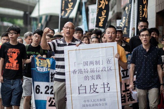 Демонстранти викрикують гасла під час ходи до Офісу представника Пекіна в Гонконзі 11 червня 2014 р. У їхніх руках велика репродукція урядового документа із Пекіна. Китай видав документ, у якому підкреслюється його контроль над Гонконгом