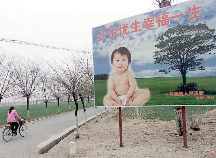 Женщина на велосипеде проезжает рядом с рекламным щитом, который поощряет семьи иметь только одного ребёнка. Щит установлен в пригороде Пекина вдоль дороги, ведущей к селу. 25 марта 2001 г. Один китайский чиновник недавно предложил внедрить в некоторых регионах разрешение иметь два ребёнка. Фото: Goh Chai Hin/AFP/Getty Images