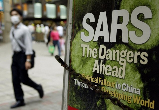 Людина в масці для захисту від атипової пневмонії SARS проходить повз газетний кіоск із заголовком новин на вулиці в Гонконзі, травень 2003 р